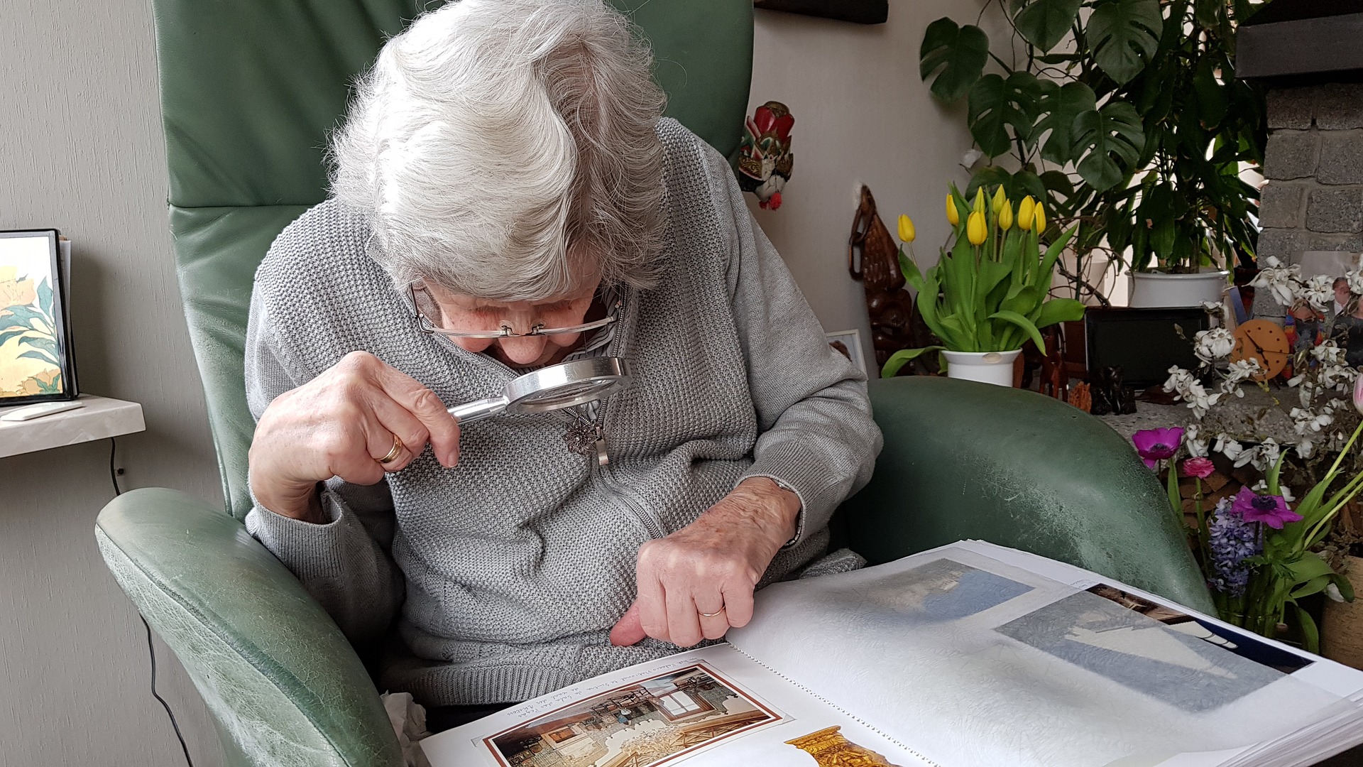 A low vision person sitting in a chair using a magnifier to read a book.